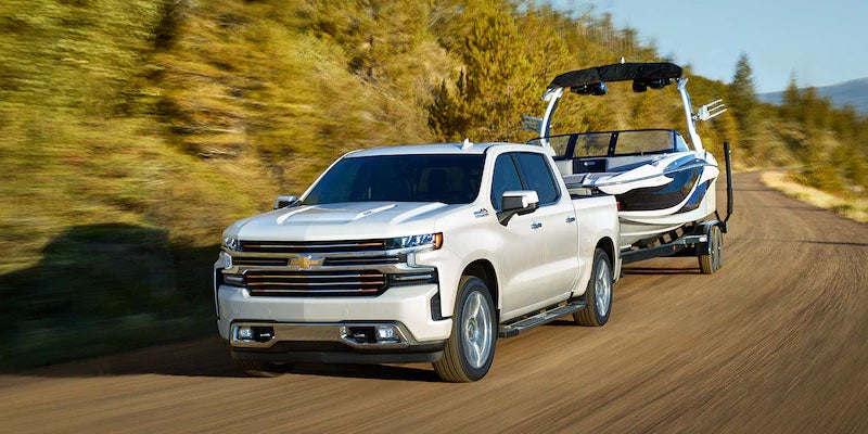 Image of a white 2022 Chevrolet Silverado driving on the road and towing a boat