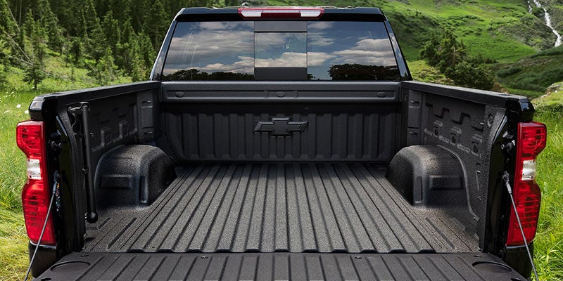 Image of open bed of a 2022 Chevrolet Silverado pickup truck, shown in a scenic outdoor setting with trees and hills in the background