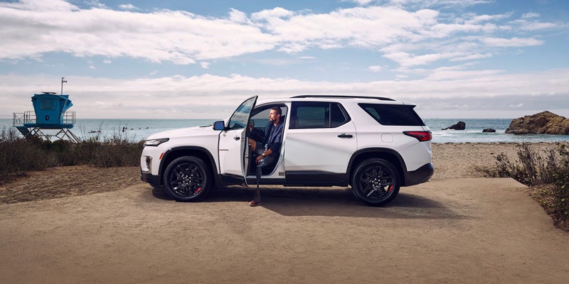 Image of a man getting out of a white color 2023 Chevrolet Traverse that parked on the lakeside