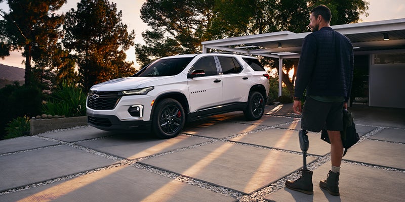 Image of a man walking toward the white color 2023 Chevrolet Traverse parked in the backyard