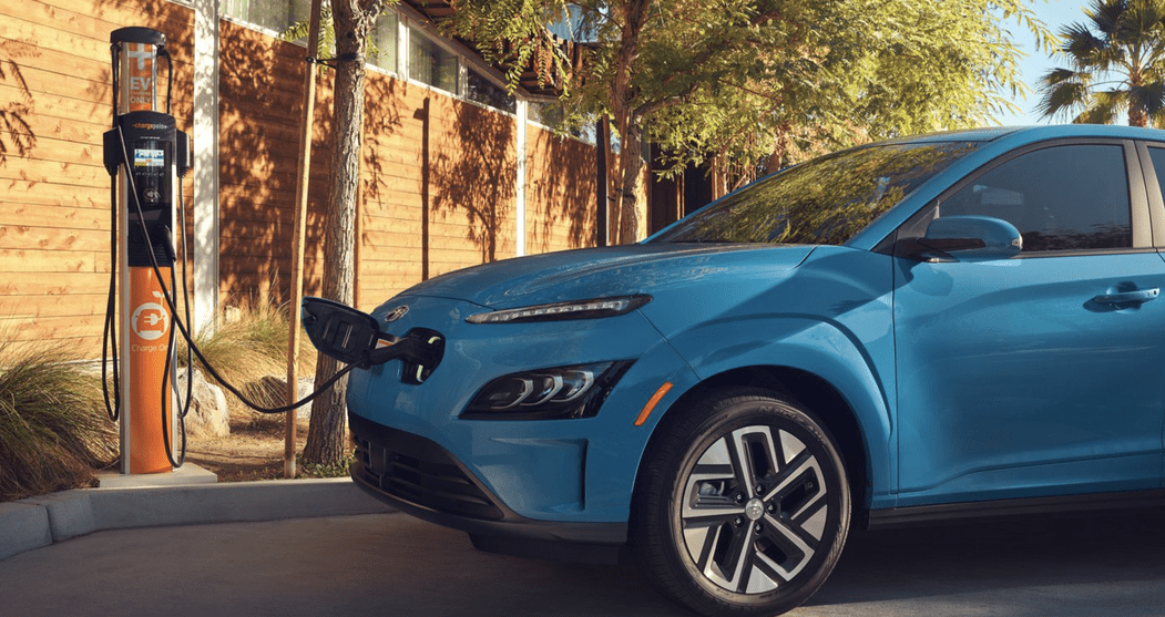 Image of blue Hyundai Kona Electric is parked in the parking lot and connected to the charging station.