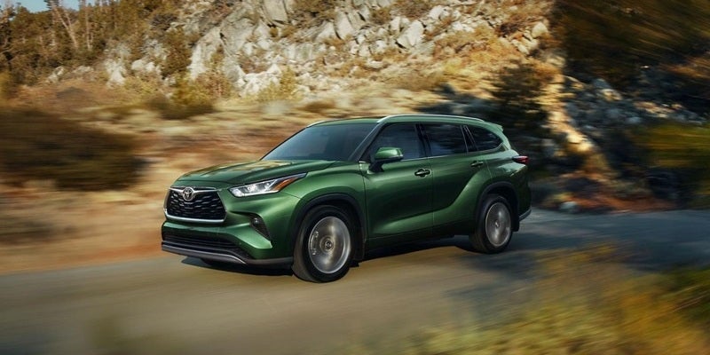 Image of a green 2023 Toyota Highlander driving on the road beside a mountain